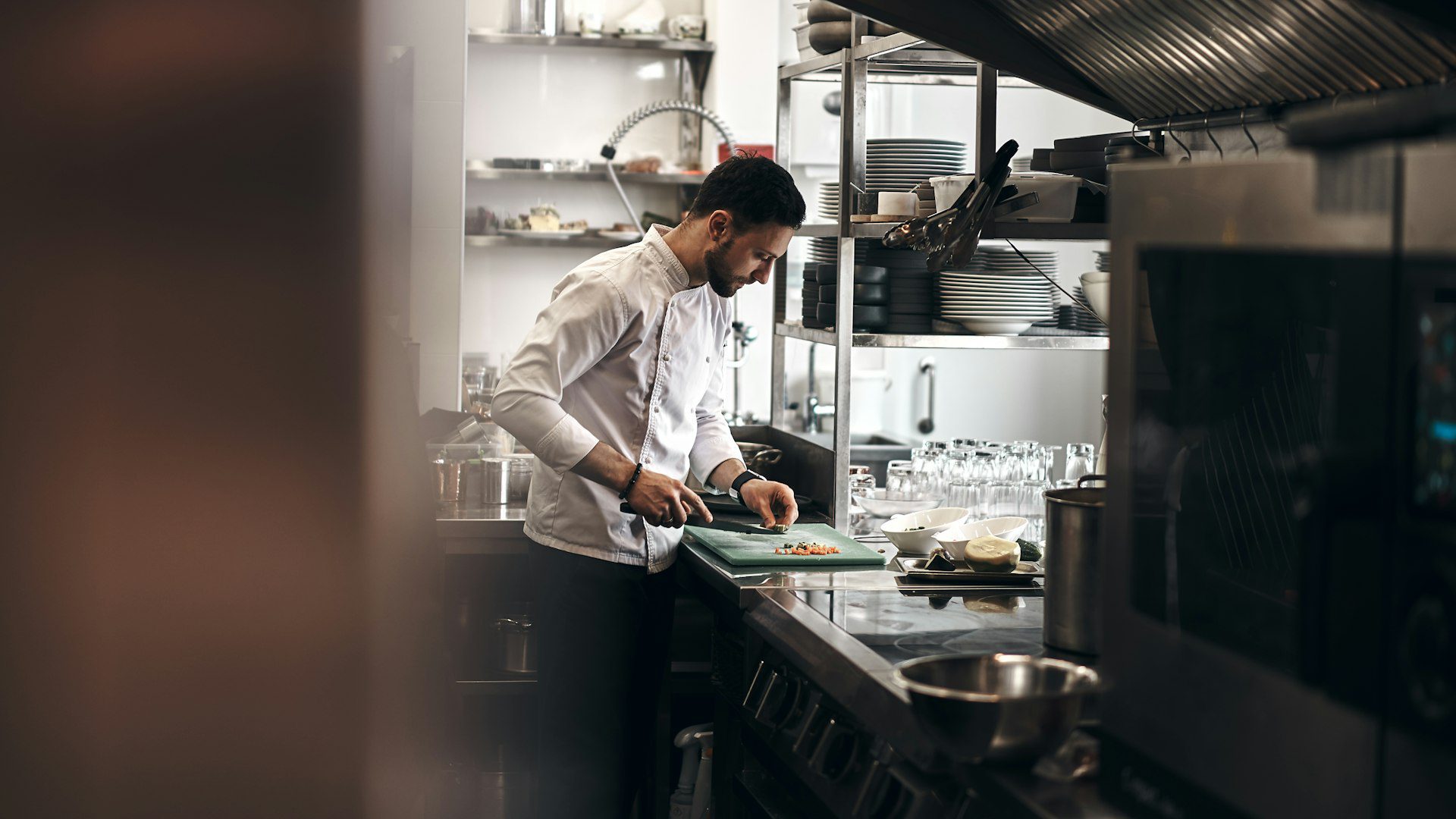 Chef preparing vegetables at a clean stainless steel prep station in a commercial kitchen